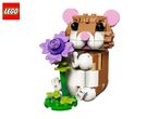 A brown and white toy hamster made of building blocks, holding a purple flower.