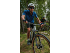 Two men mountain biking through a forest, wearing helmets, sunglasses, and athletic apparel.