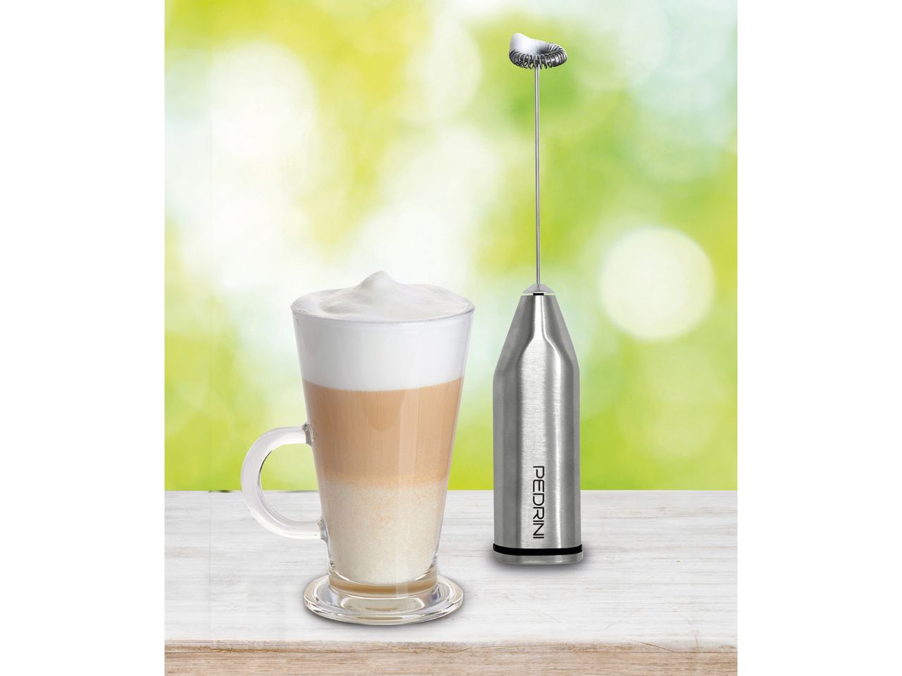 Un cappuccino cremoso in una tazza di vetro accanto a un frullino montalatte
