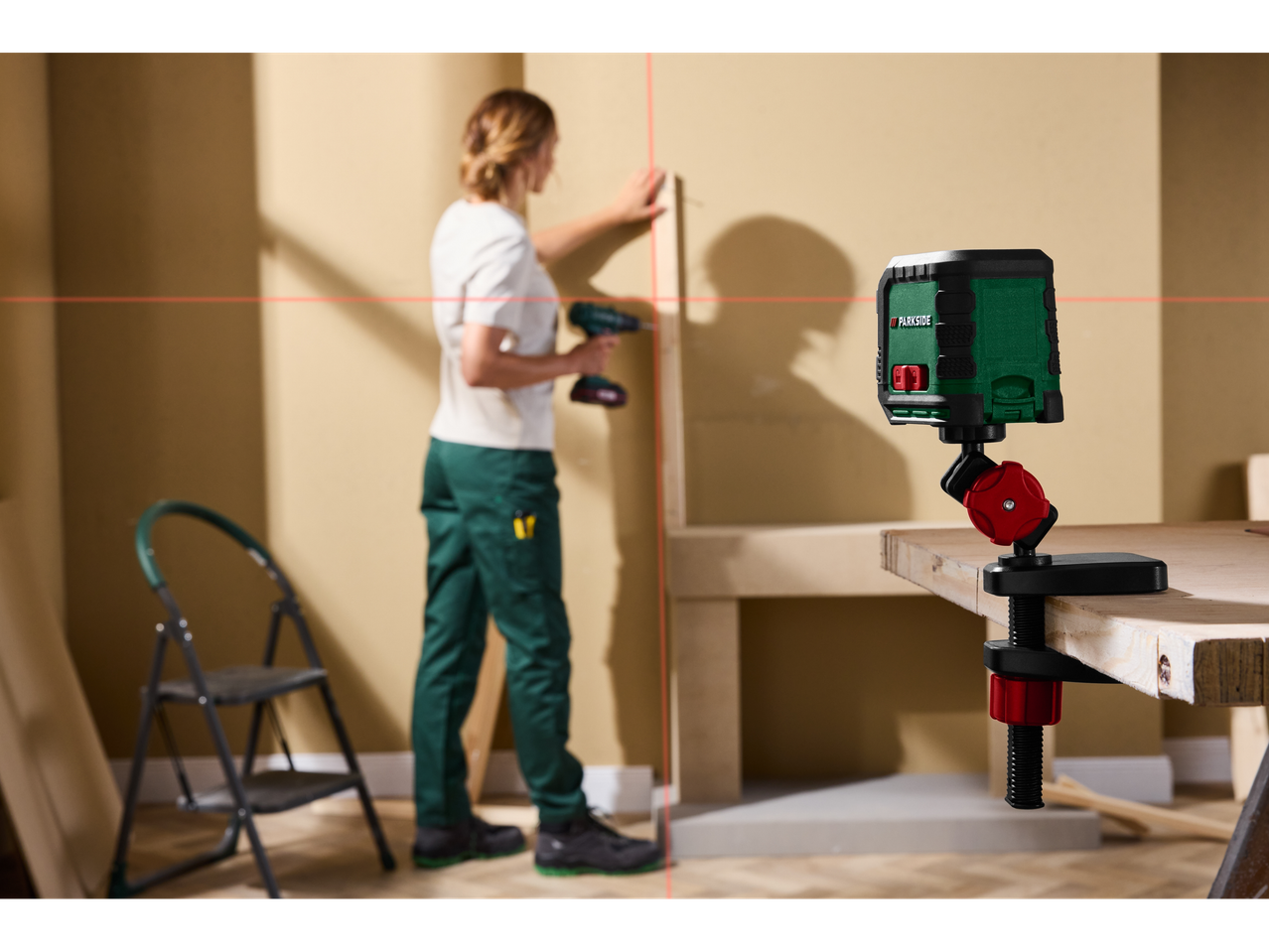 Mulher usa laser de linhas cruzadas na parede, enquanto um medidor de distância a laser está preso a uma mesa.