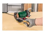 Bench grinder sharpening a chisel, with a person's gloved hand holding the tool.