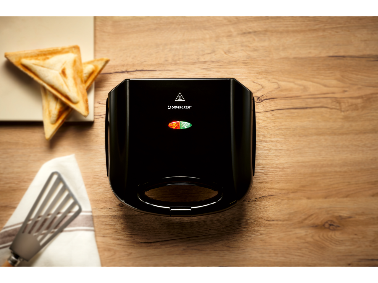 Sandwich-uri triunghiulare prăjite lângă un toaster SilverCrest negru pe o masă din lemn.