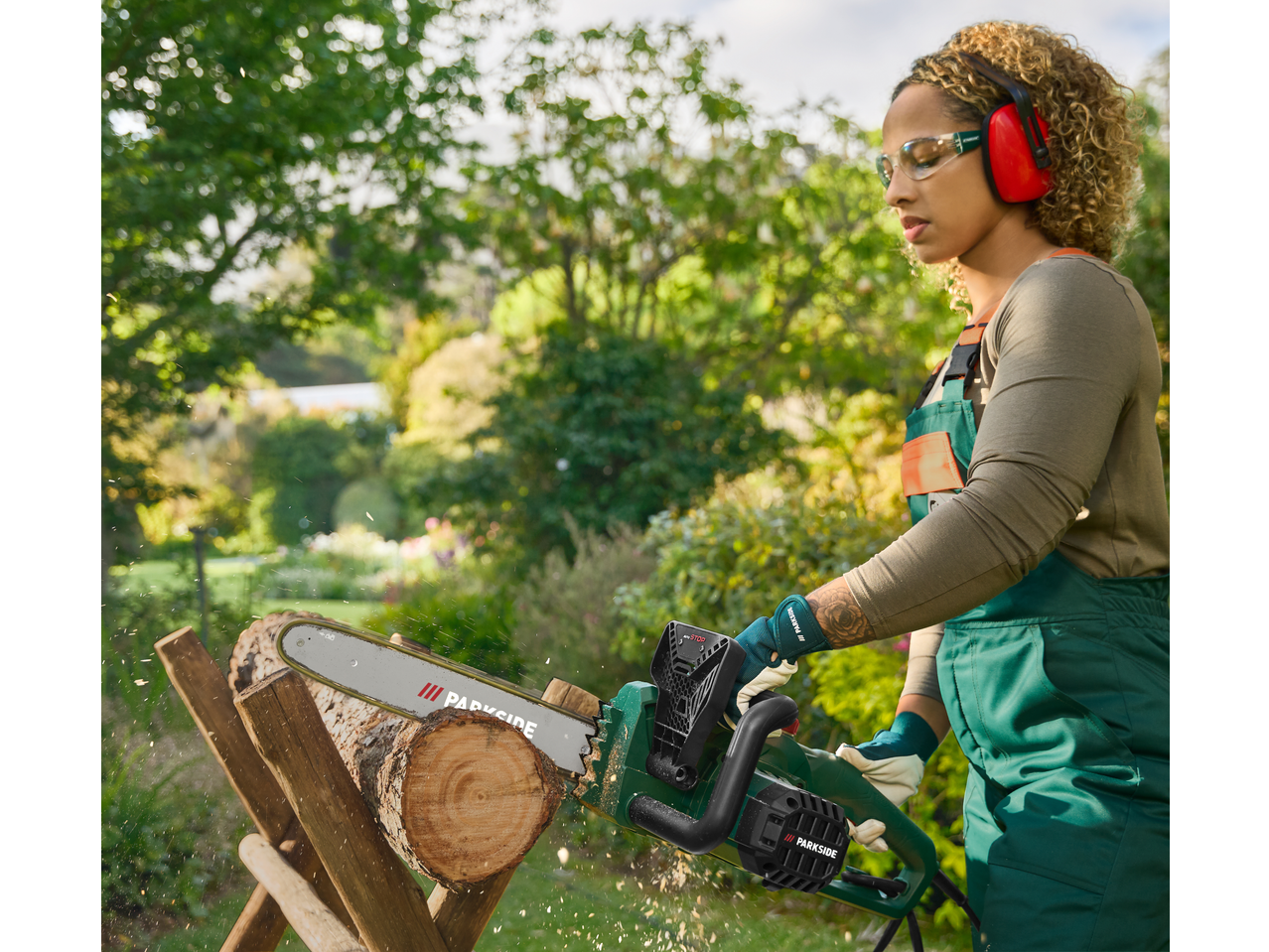 Woman cutting wood with a chainsaw, wearing safety glasses and ear protection.