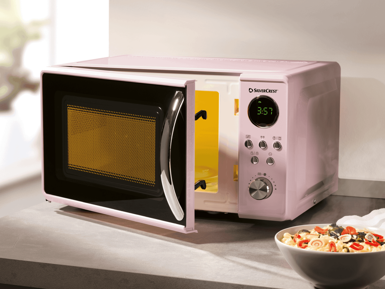 Ein rosafarbener Retro-Mikrowellenherd der Marke SilverCrest steht auf einer Küchenarbeitsplatte neben einer Schüssel Pasta.