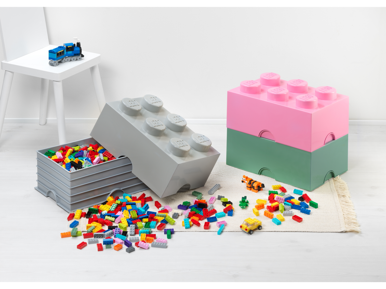 Lego® klotside hoiukarbid hallis, roosas ja rohelises värvitoonis koos laiali pillutatud klotsidega.