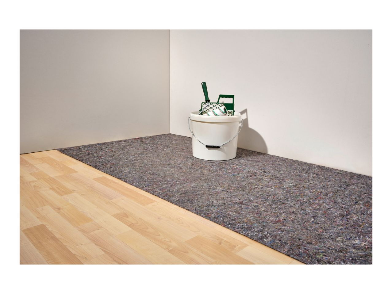 A room with a paint bucket, roller, and floor protection fleece on a wooden floor.