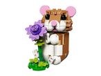 A brown and white toy hamster made of building blocks holding a purple flower.