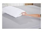 A hand adjusting the filling of a white quilted pillow on a grey bed.