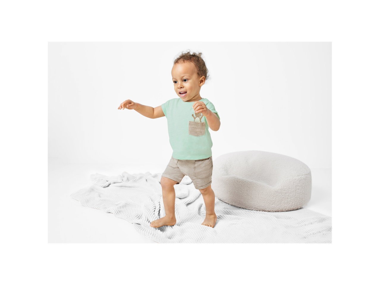 Bebe u mintno zelenoj majici i bež hlačicama na mekom bijelom tepihu.