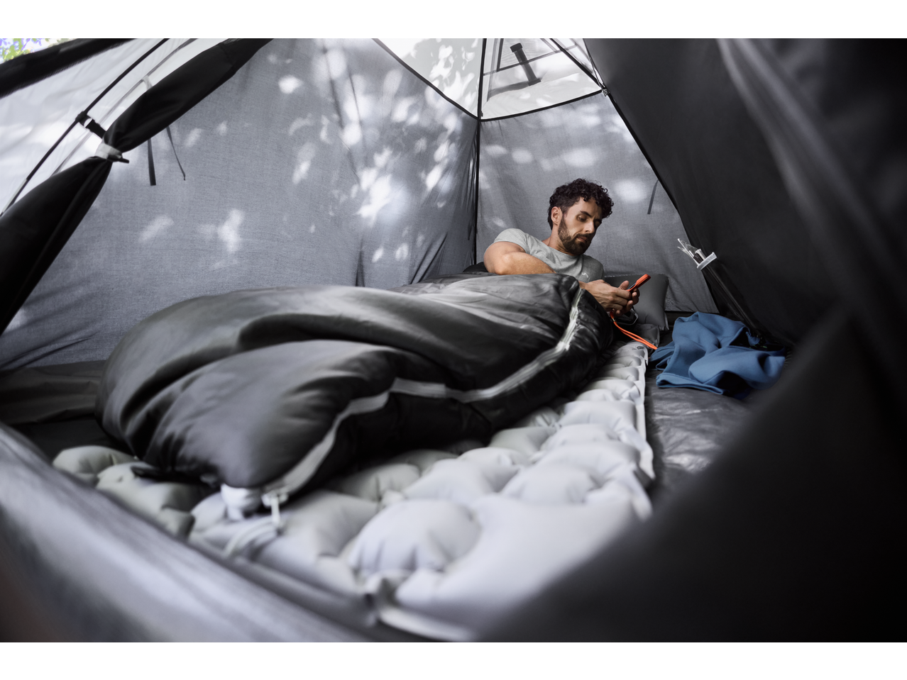 Man relaxing in a CRIVIT Camping Tent, using his phone while lying on a sleeping pad.