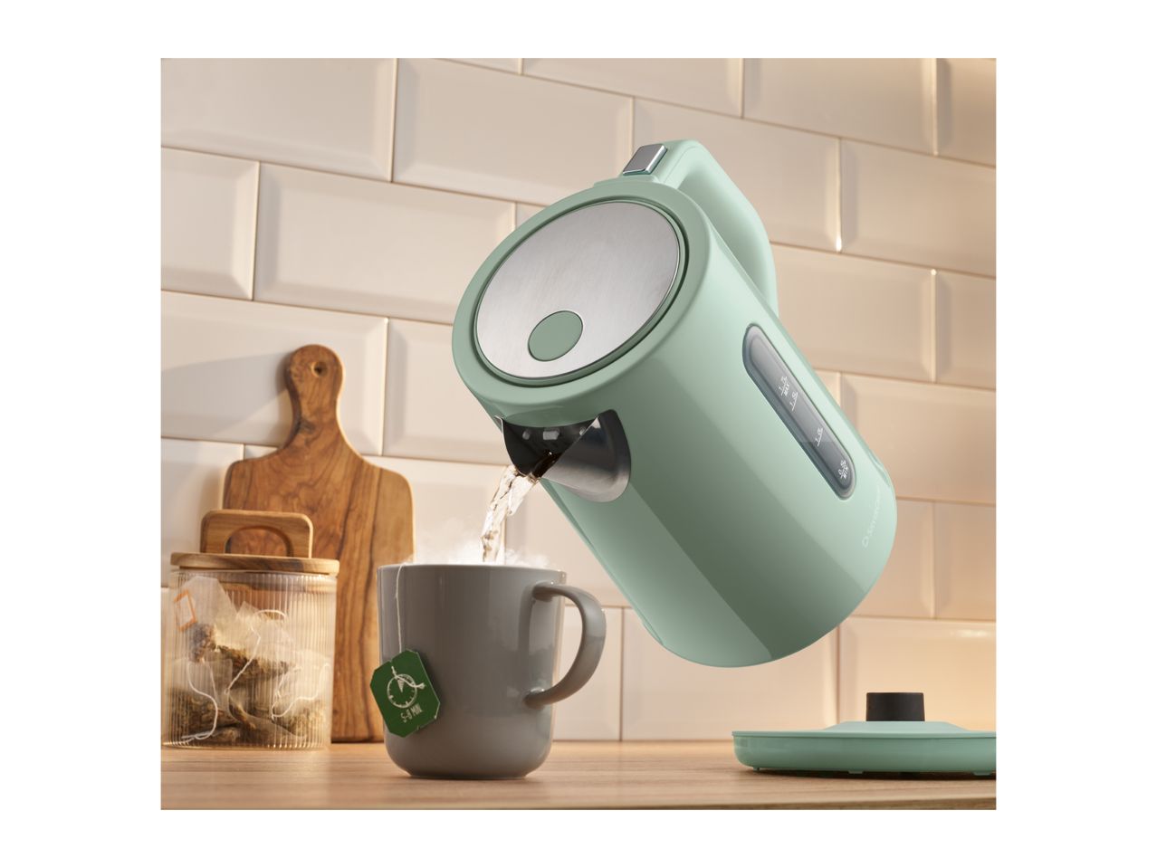 Mint green electric kettle pouring hot water into a grey mug with a tea bag.