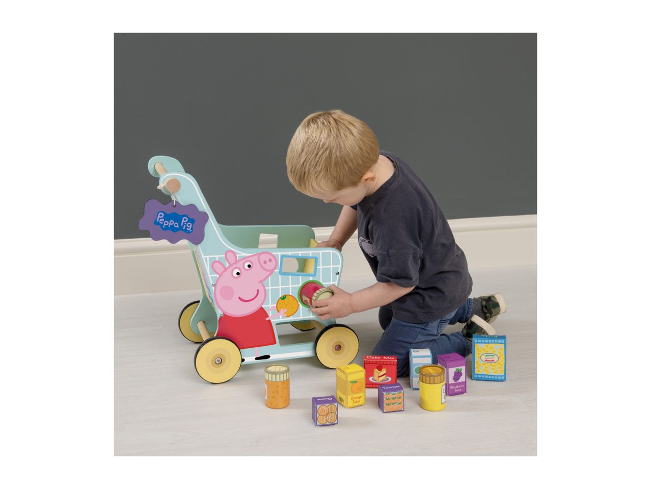 Toddler playing with a wooden shopping trolley featuring a pig character and toy food items.
