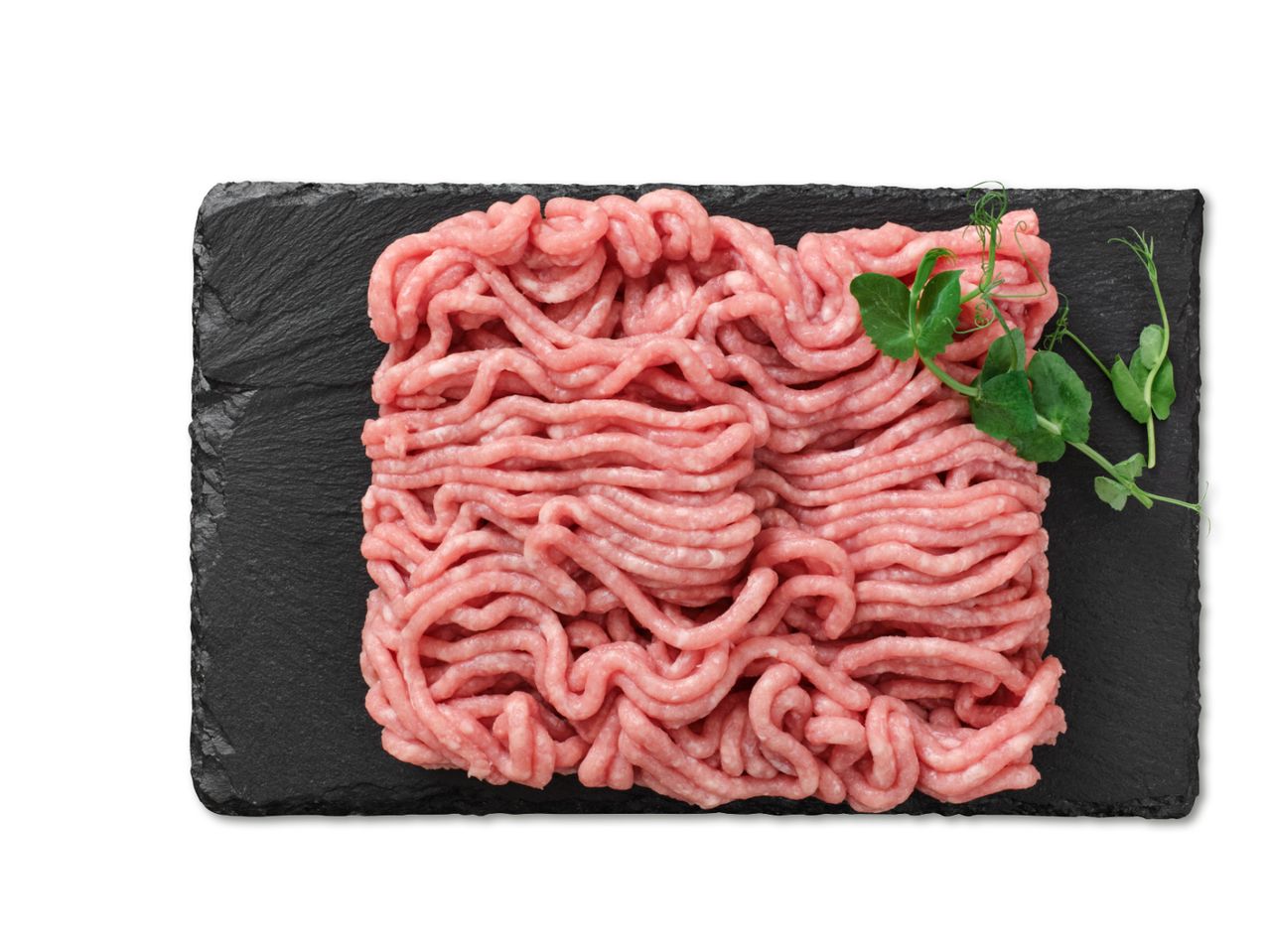 Toores hakkliha tükk mustal kildal koos värskete hernestega.