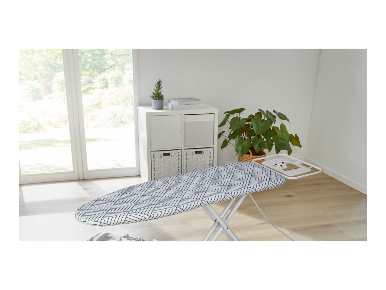 Ironing board with a geometric pattern cover in a bright room with a large window.