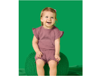 Happy baby girl in a pink muslin two-piece set, sitting on a green knitted pouf.