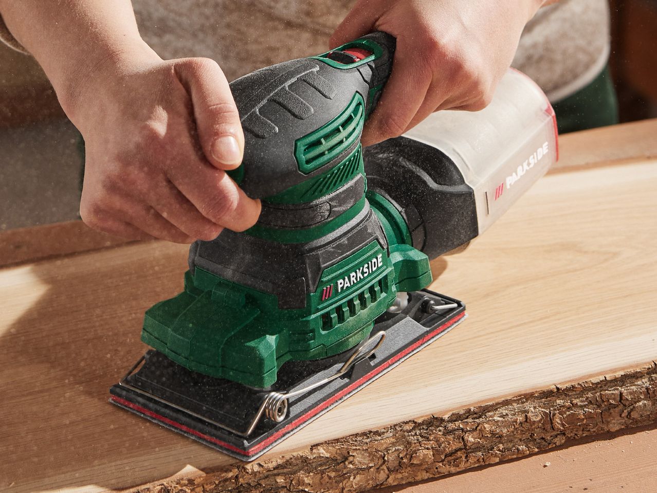 A person uses a Parkside brand electric sander on a piece of wood.