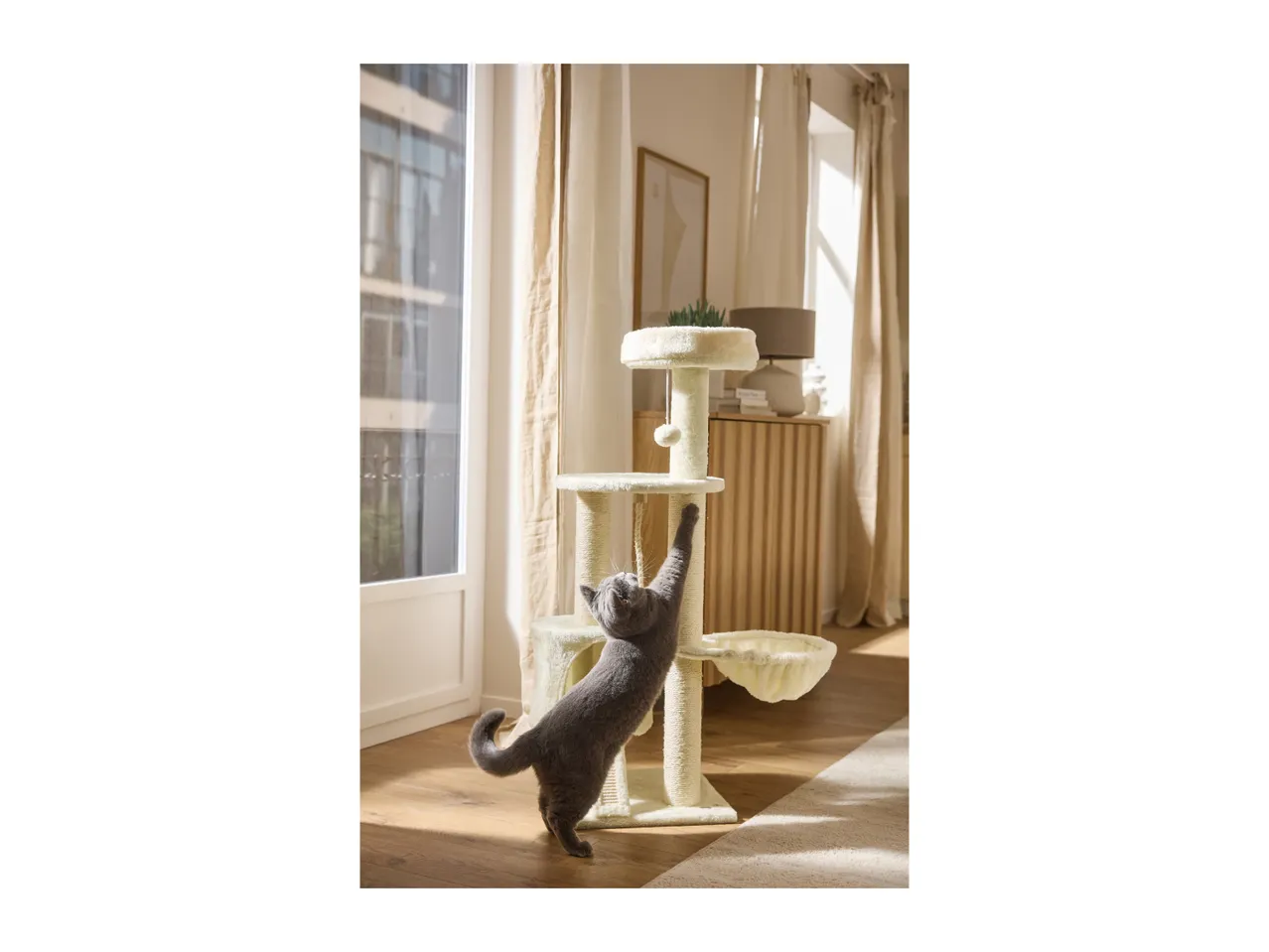 A grey cat stretching up to scratch a cream-coloured multi-level cat tree.
