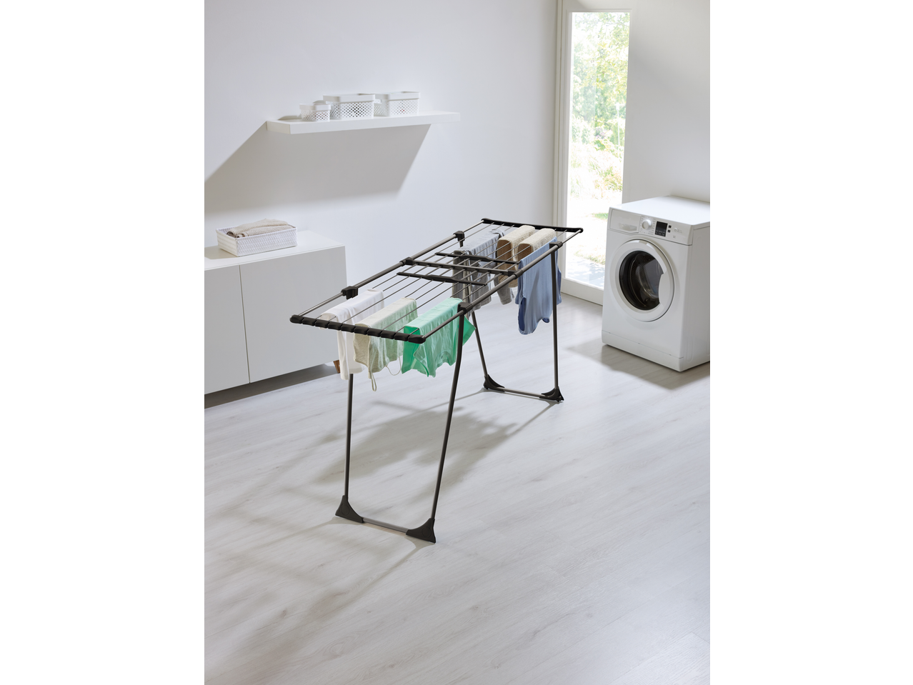 Laundry room with a clothes drying rack holding various garments, a washing machine, and storage.