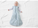 Baby in a light blue polka dot sleep sack on a white blanket.