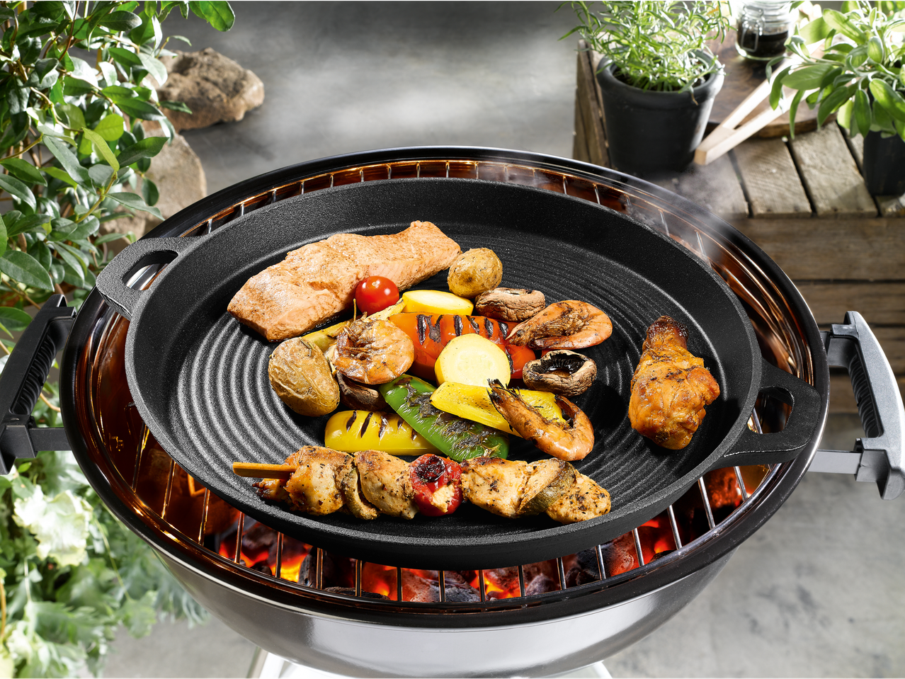 Ливена гвоздена роштиљ тава са лососом, шкампима, пилетином и поврћем се пече на угљеном роштиљу.