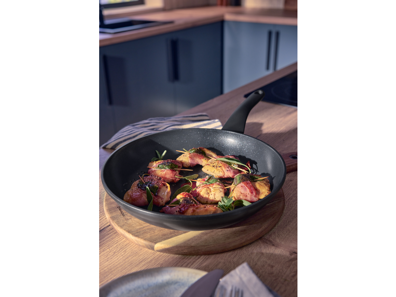 Pancetta-wrapped chicken with sage in a frying pan on a wooden board in a kitchen.