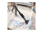 A person vacuuming colorful confetti from a cream-colored rug with a stick vacuum.