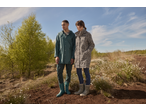 Twee mensen in regenjassen, één in een groene trenchcoat en de ander in een trenchcoat met luipaardprint, staan buiten.