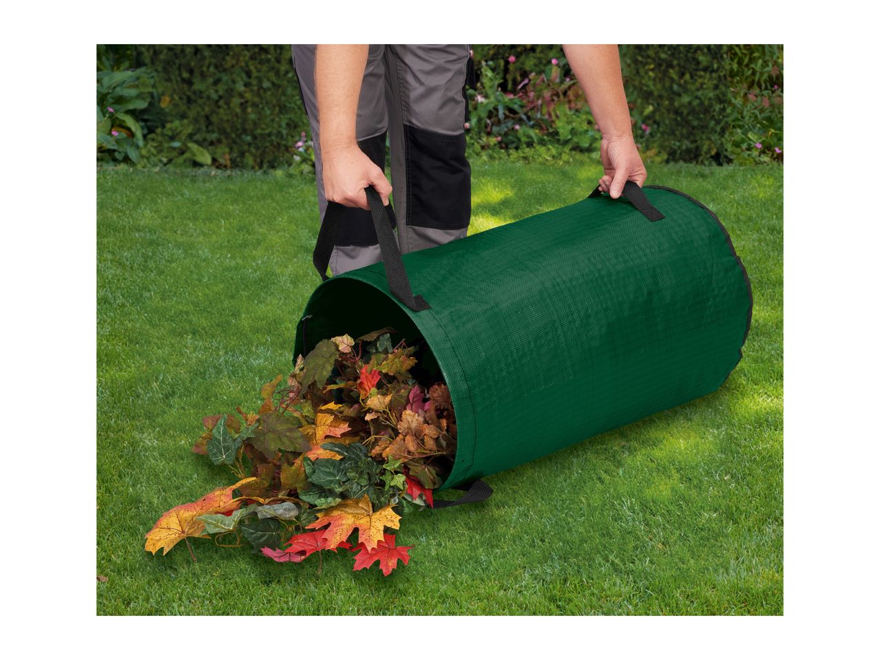 Person emptying a green garden waste bag filled with colorful autumn leaves onto a lawn