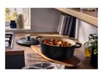 Black oval cast iron pot with stew on a wooden kitchen counter next to a stove.