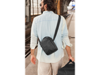 Homem numa estação de comboio com uma mala de ombro e uma mala de viagem.