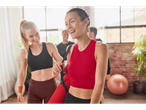 Două femei râd în timp ce poartă haine de sport și saltele de yoga.