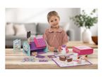 A young girl playing with a toy cafe set, featuring a cash register, cakes, and tea set.