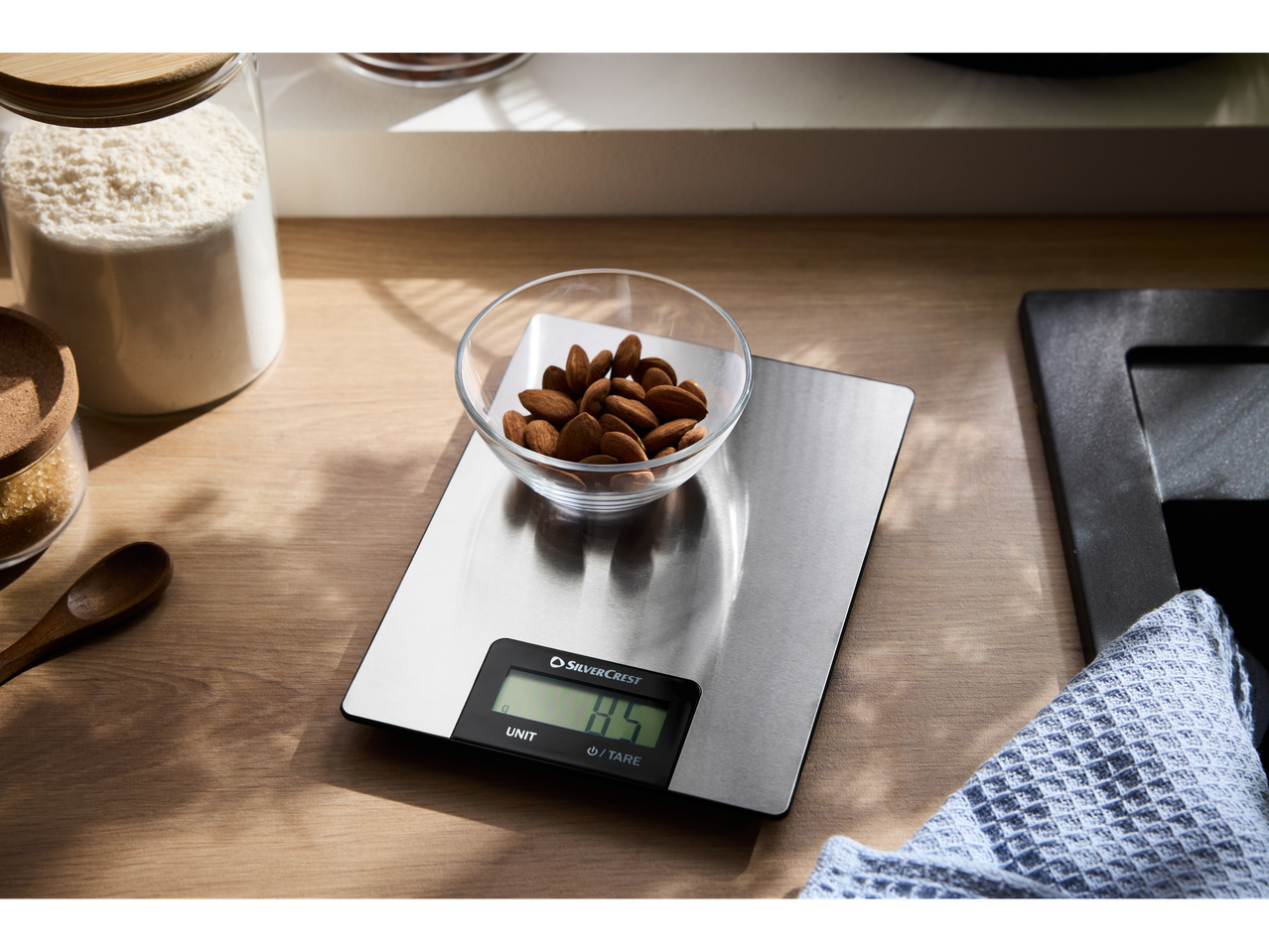 Cântar de bucătărie digital Silvercrest cu un bol de migdale, făină și zahăr pe un blat de lemn.