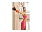 Woman in pink activewear using an orange resistance band for exercise indoors.