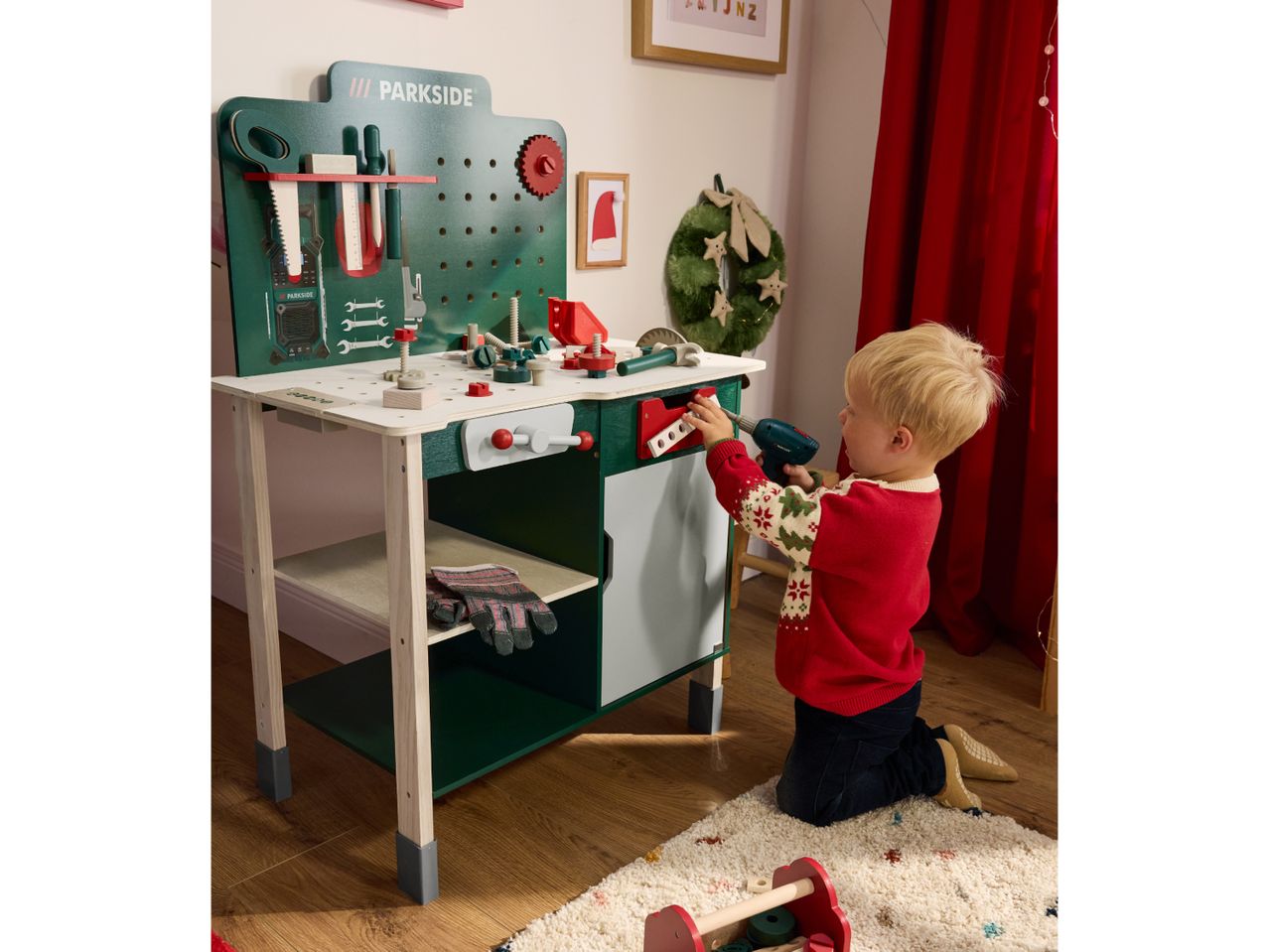 A child playing with a green toy workbench, featuring various tools and accessories.