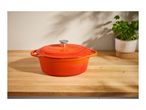 An orange Le Creuset Dutch oven on a wooden countertop with a potted basil plant.