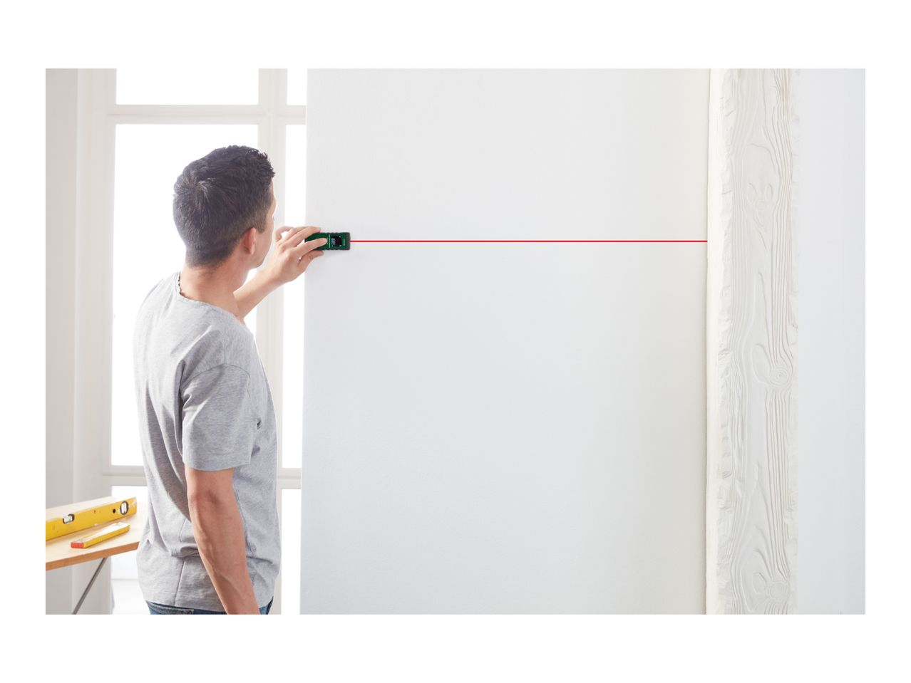 Man using a laser level to project a red line on a white wall.