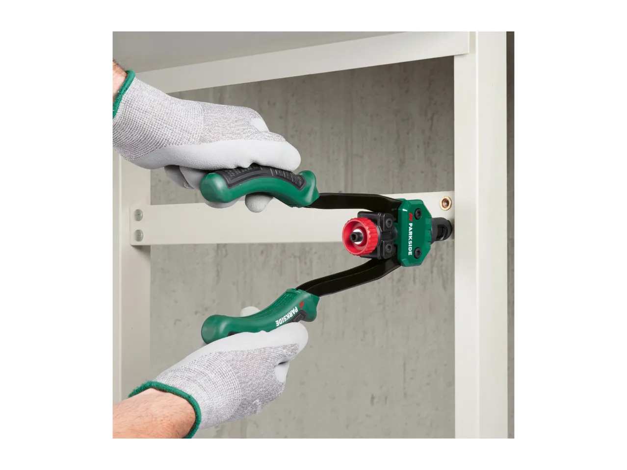 Hands in work gloves using a rivet gun to attach a metal shelf bracket.