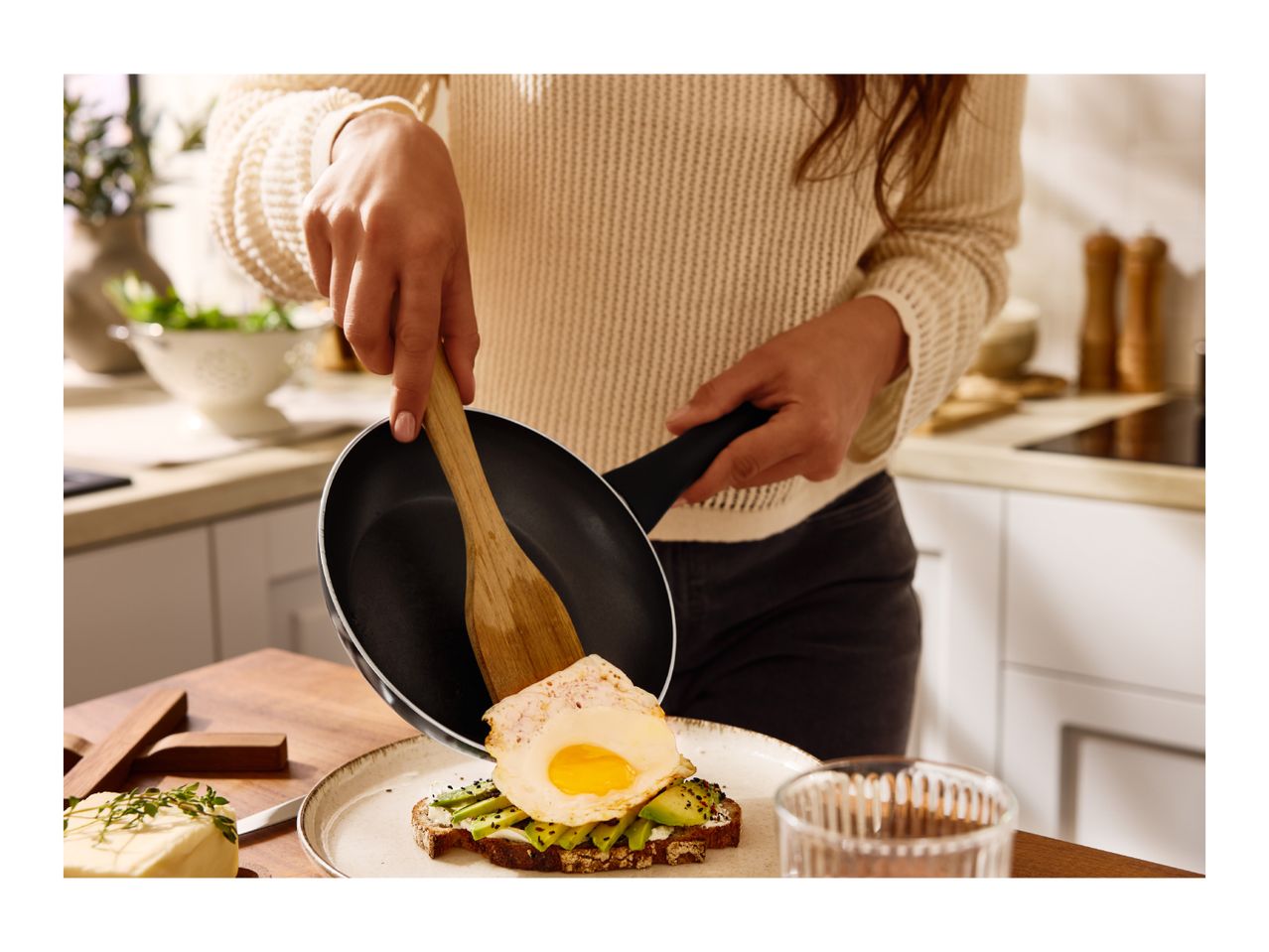 A person serving a fried egg from a frying pan onto avocado toast.