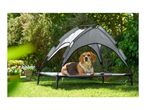 Beagle dog resting on a raised dog bed with a sun canopy in a garden.