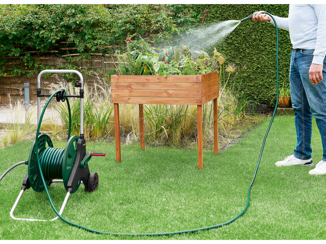 PARKSIDE kolica za crijevo zalijevaju povišenu vrtnu gredicu u zelenom vrtu.