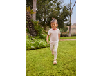 Smiling girl in a Lupilu Kids' T-Shirt and heart-patterned leggings running on grass.