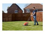 Man mowing a green lawn with a red and grey lawnmower in a garden with a wooden fence.