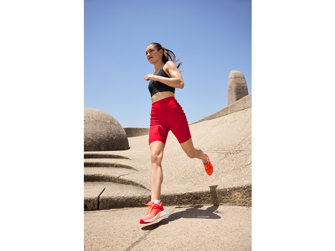 Woman running in red cycling shorts and black sports bra on a sunny day.