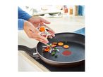 Hands adding sliced vegetables to a frying pan on a hob