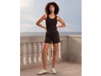 Mulher de top preto e calções, de pé numa varanda com vista para o mar.