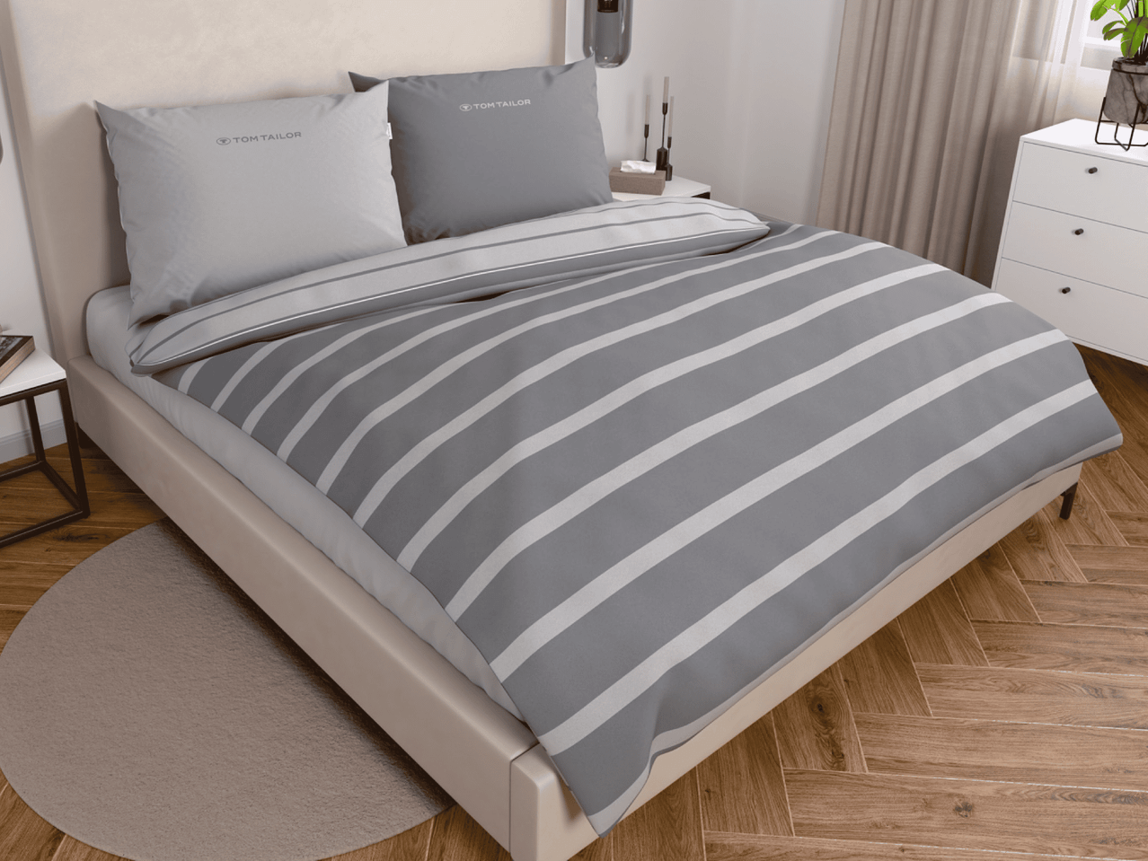 Graue Bettwäsche mit weißen Streifen und Tom Tailor Kissen auf einem Bett in einem Schlafzimmer.