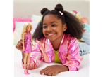 A smiling girl in a pink jacket plays with a Barbie doll in a matching pink dress.