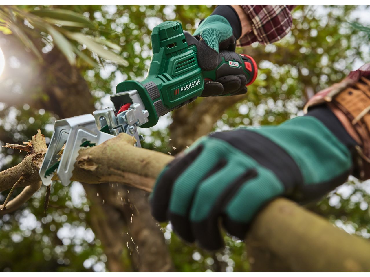 Un giardiniere usa un Seghetto ricaricabile PARKSIDE® per potare un ramo di albero.