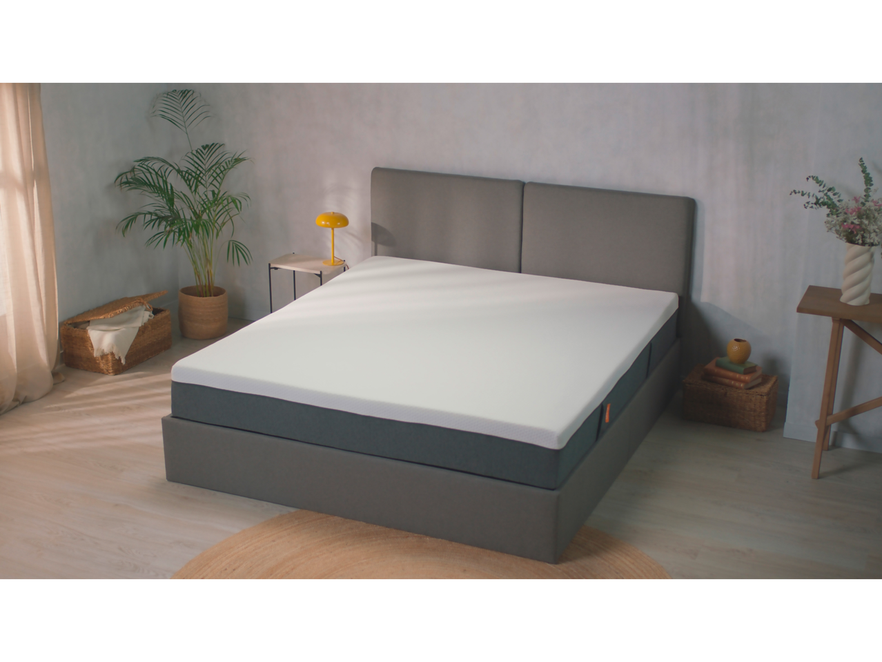 A gray upholstered bed frame with a white mattress sits in a minimalist bedroom.